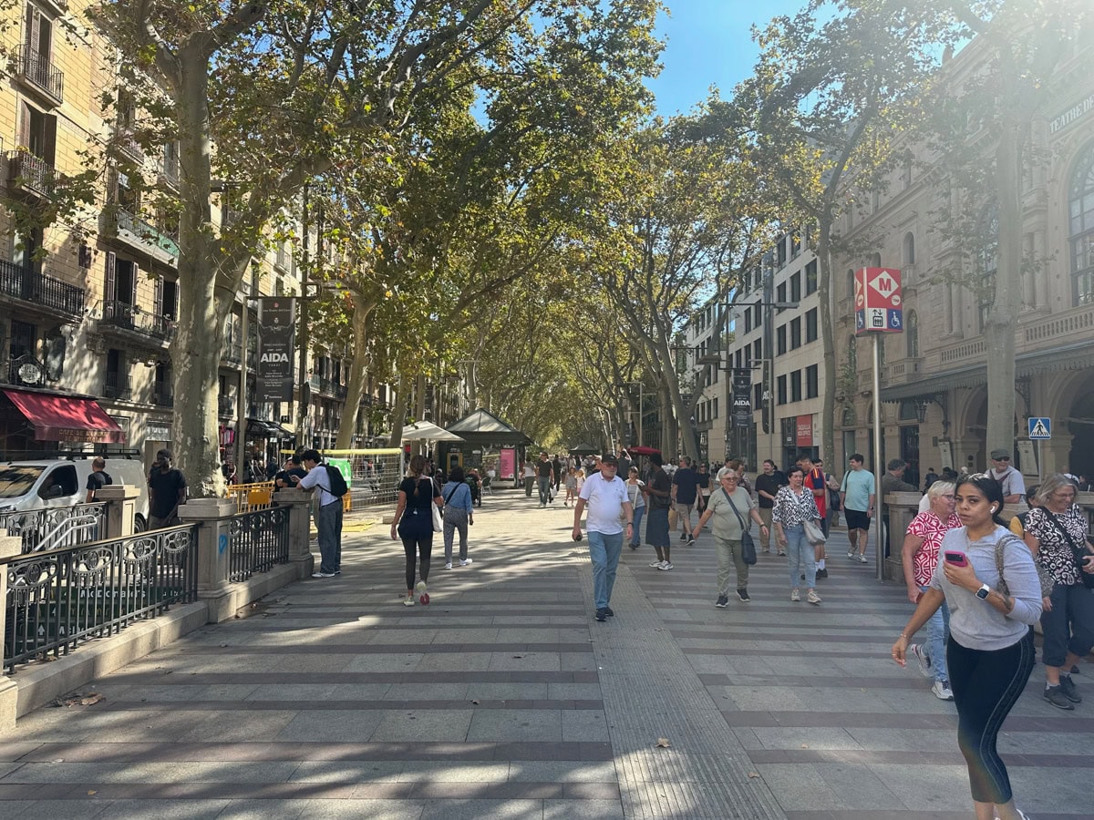 People walking in Barcelona under the trees near the entrance of an underground subway.