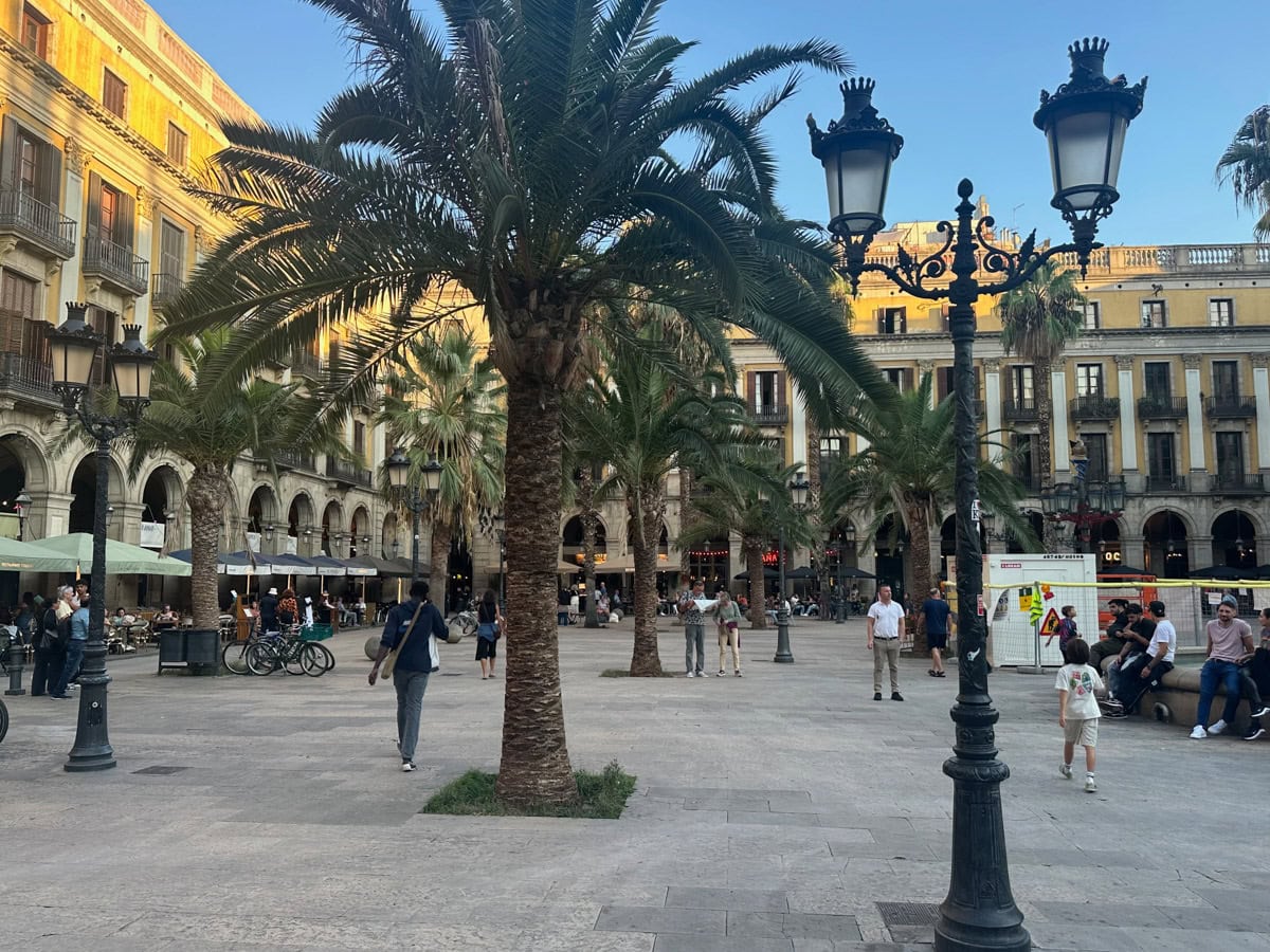 A square in Barcelona with people, bicycles, lamppost, trees, and more.