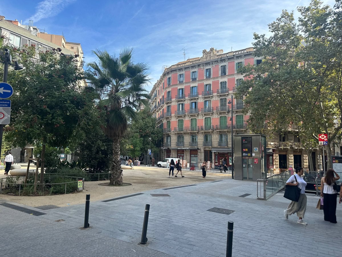 Apartment building in Barcelona, Spain surrounded by trees and a square with an entrance to a underground train.