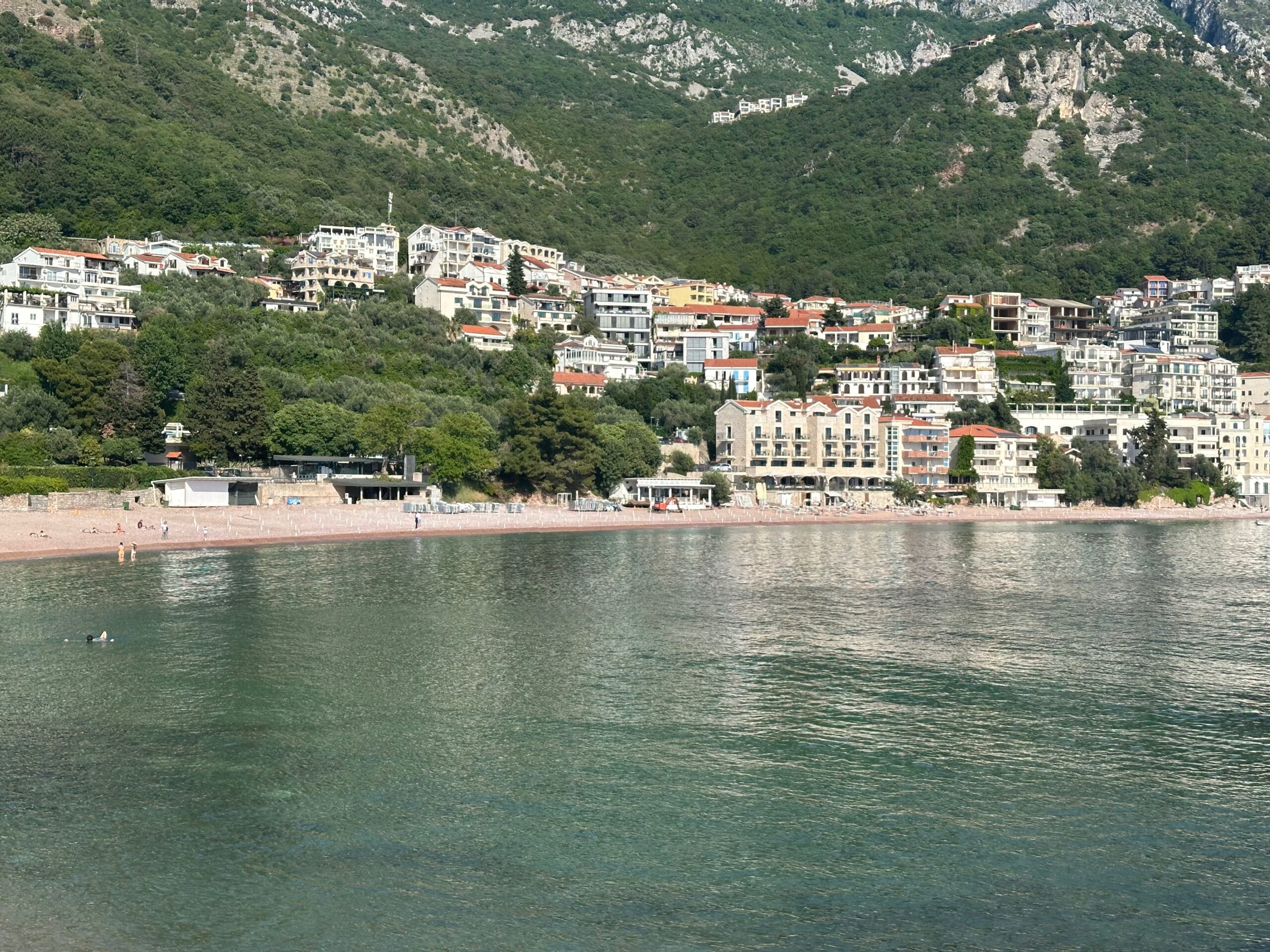 View of the coastal town of Sveti Stefan with a beach, small residential blocks of flats and hills in the background