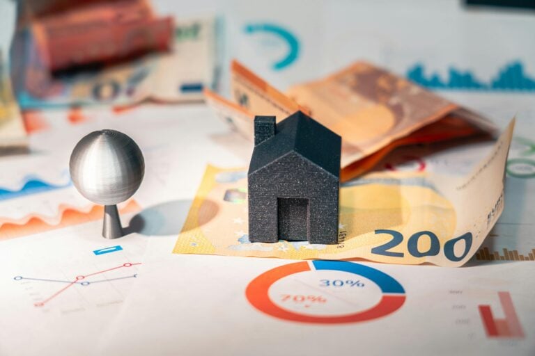 A little house figure sitting on a cash bill around paperwork.