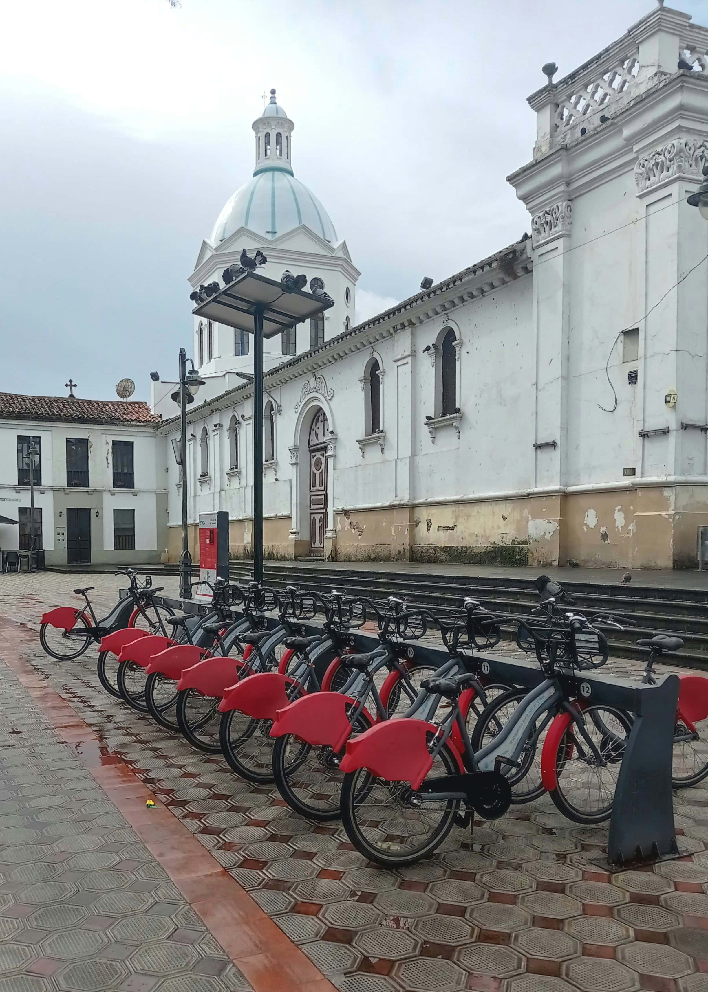 Rental bikes lined up in a central square in Cuenca, Ecuador with historical buildings behind them